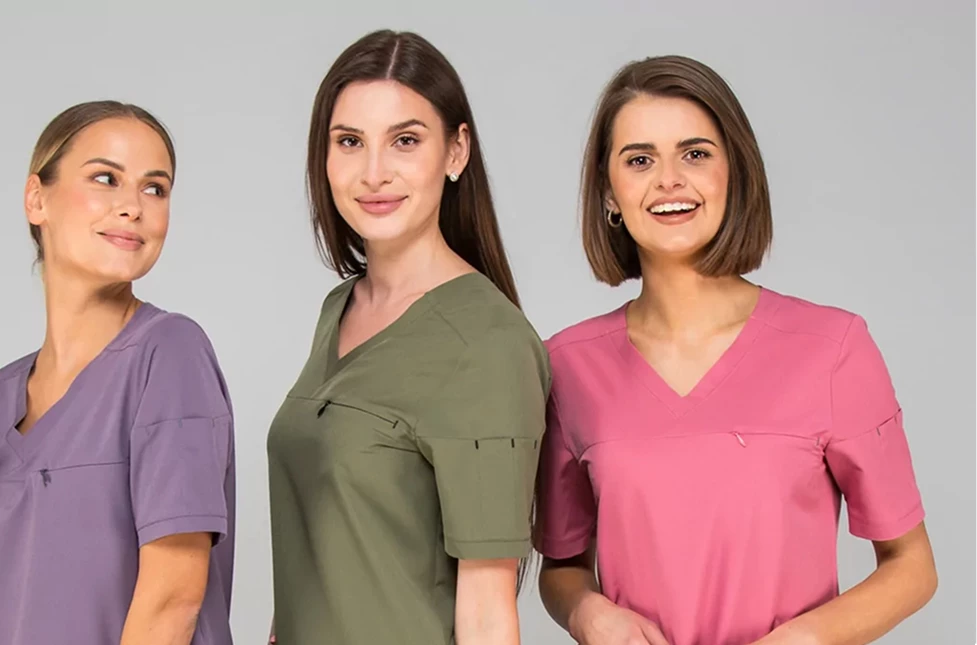 Trzy uśmiechnięte kobiety w kolorowych uniformach medycznych – fioletowym, oliwkowym i różowym.